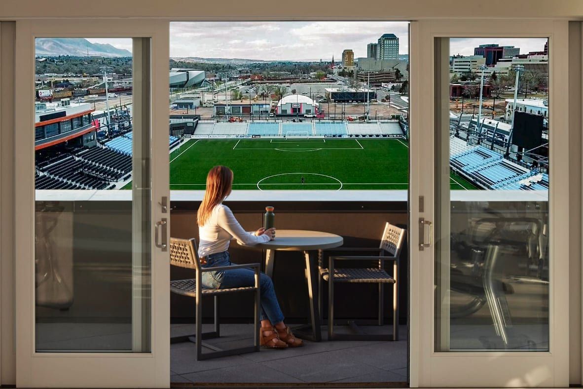 A woman is sitting at a table looking out a window at a soccer field at The Experience at Epicenter