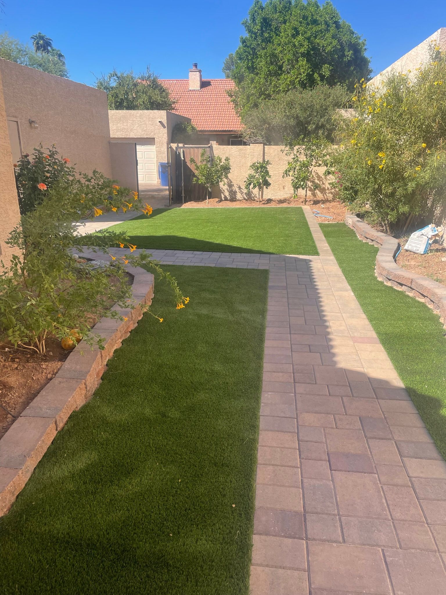 A brick walkway leading to a lush green yard with a house in the background.