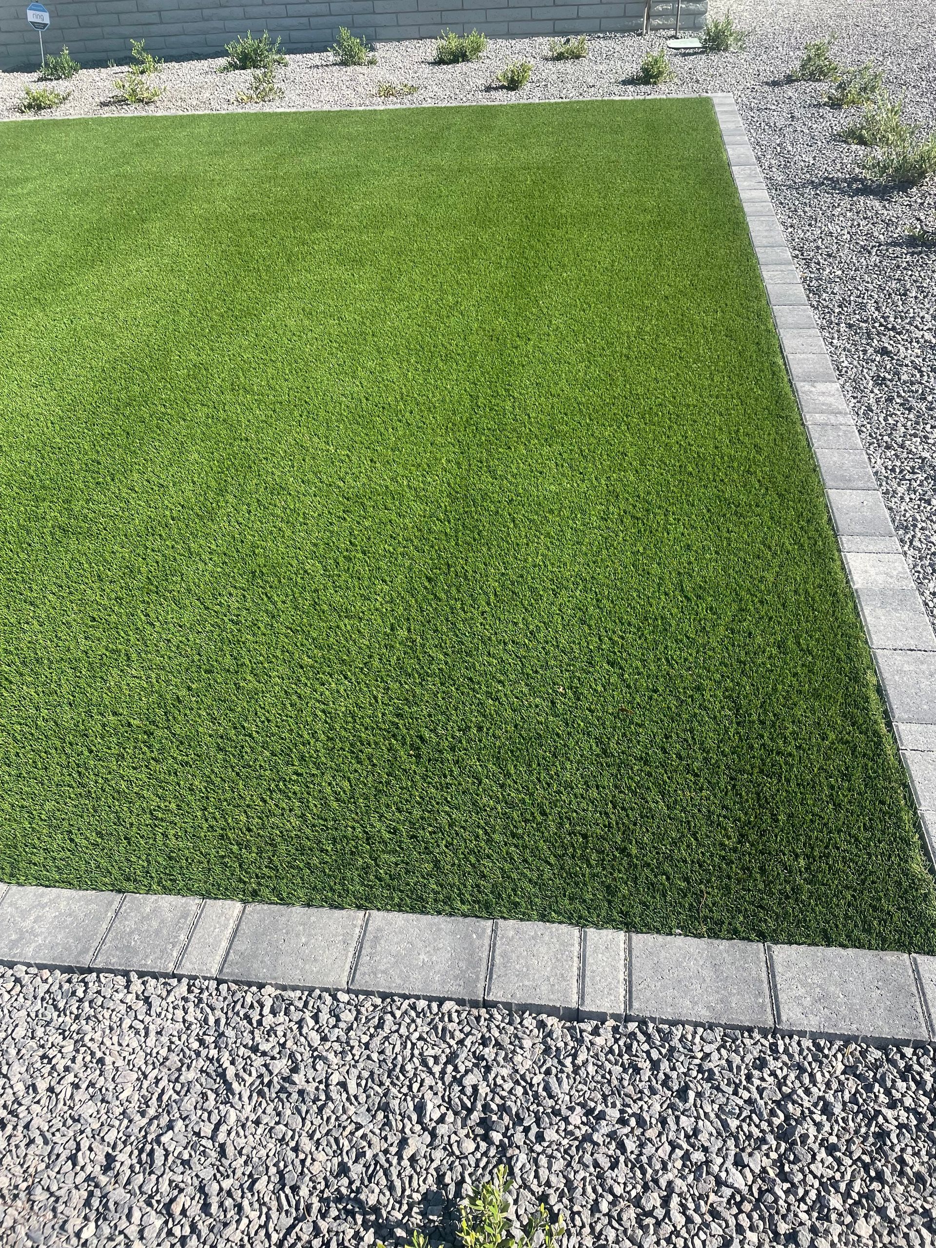 A lawn with a brick border and gravel in the background.