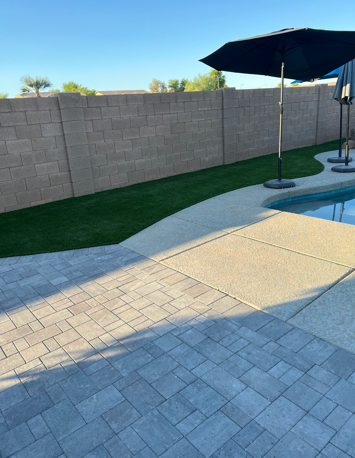 A black umbrella is sitting on a patio next to a pool.