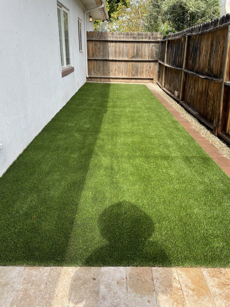 There is a shadow of a person on the grass in the backyard.