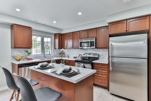 A kitchen with reddish-brown wood cabinetry, white quartz or stone countertops, and stainless steel appliances including a