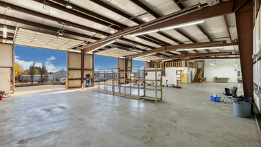 Empty warehouse interior with exposed beams, concrete floor, and a worktable near an open loading door.