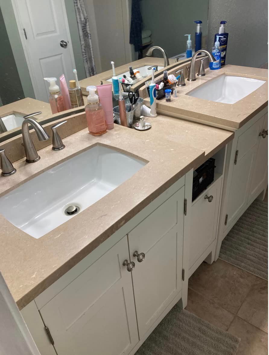 White bathroom vanity with two sinks, cluttered countertop, and a large mirror.