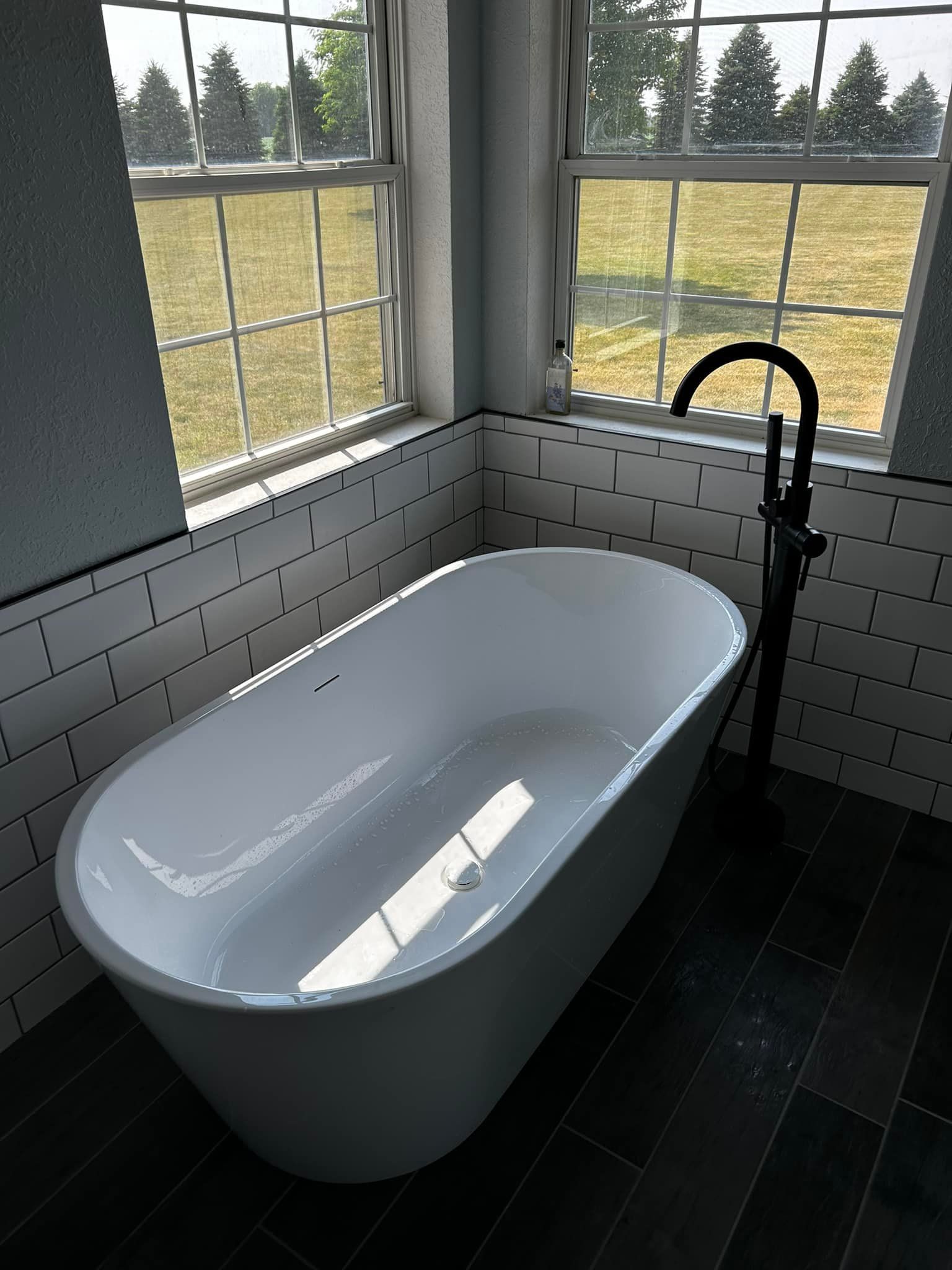 Freestanding white bathtub by a window with black faucet in a bathroom with black and white tiles.