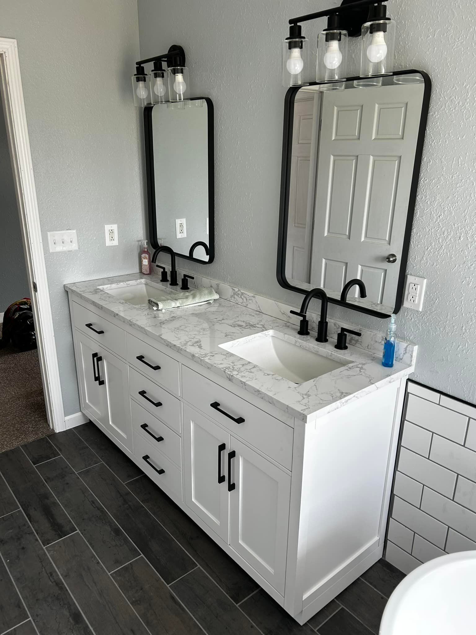 A modern bathroom with a white double vanity, black fixtures, and silver accent walls.