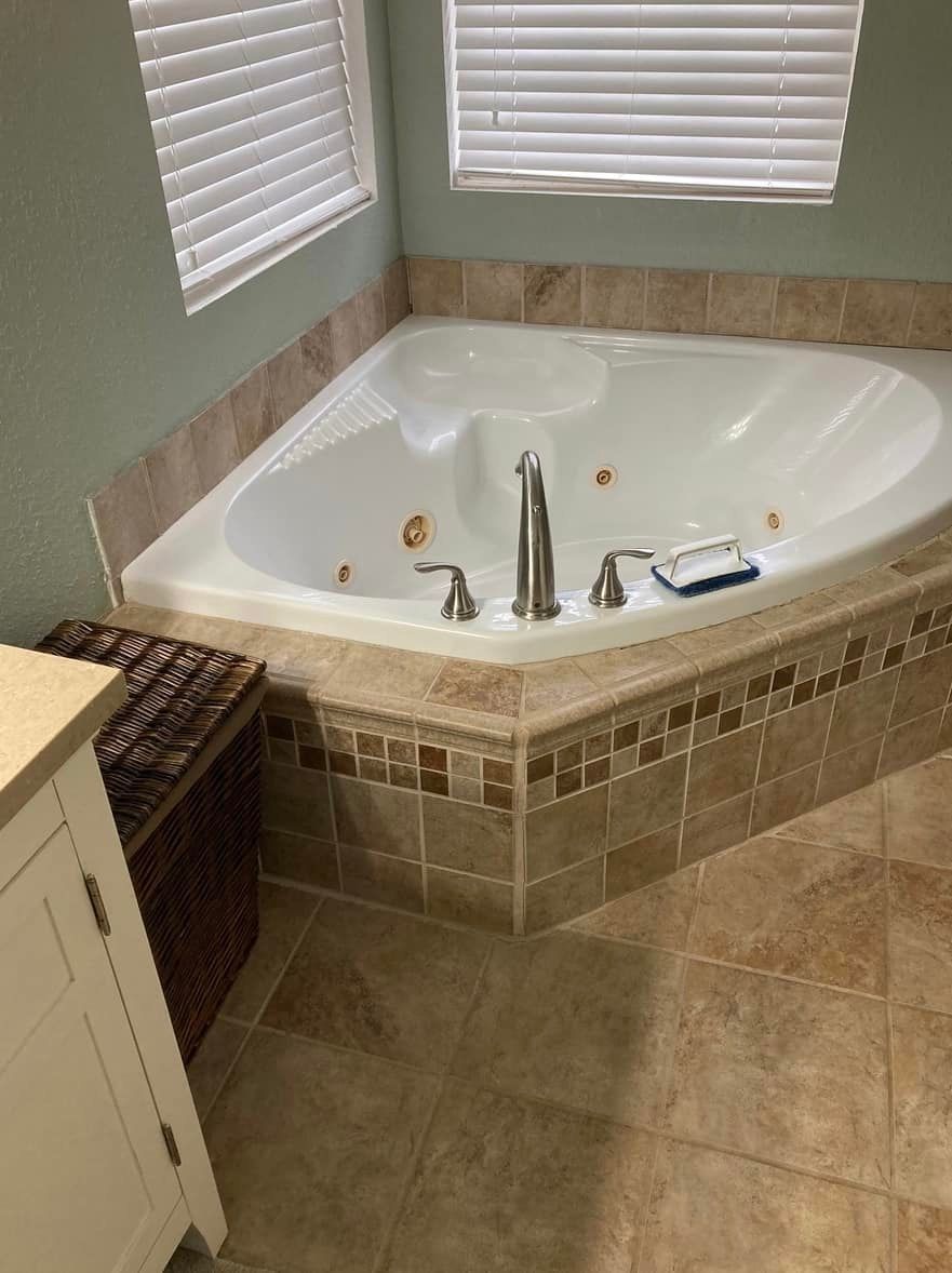 A corner whirlpool tub in a bathroom with beige tile, a window, and a vanity.
