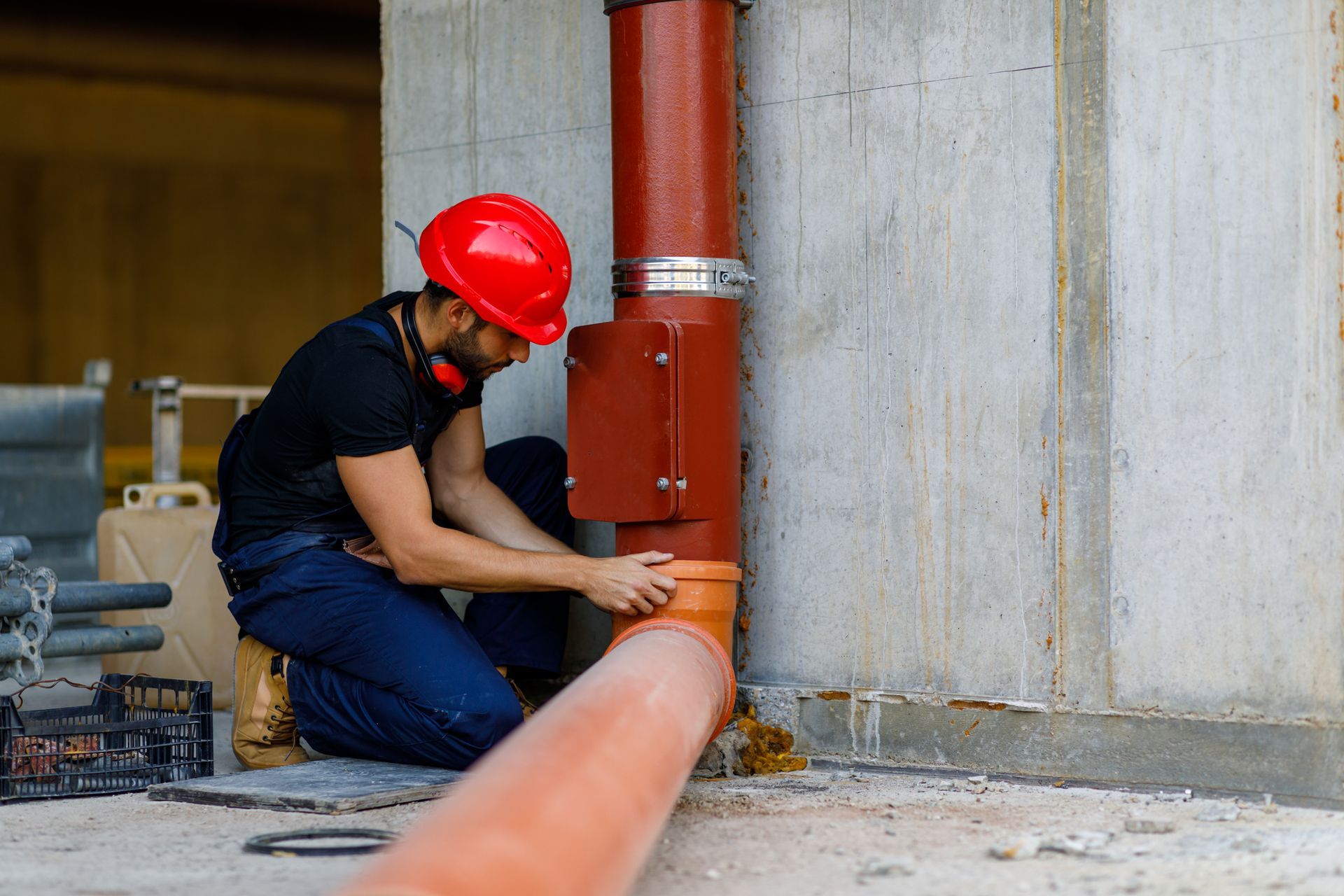 A man in a red hard hat is installing a pipe on a construction site.