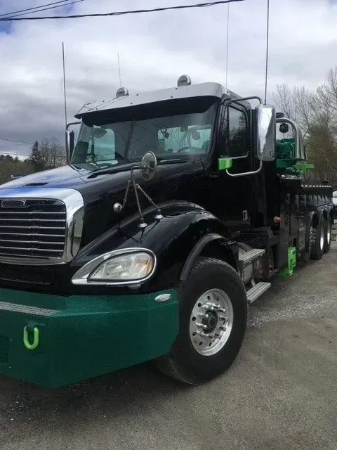 Black and green semi-truck with silver accents. It has a large grill and multiple antennas parked outside.