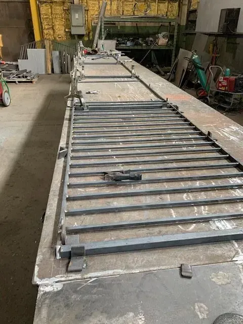 Metal gate being constructed on a long metal surface in a workshop.
