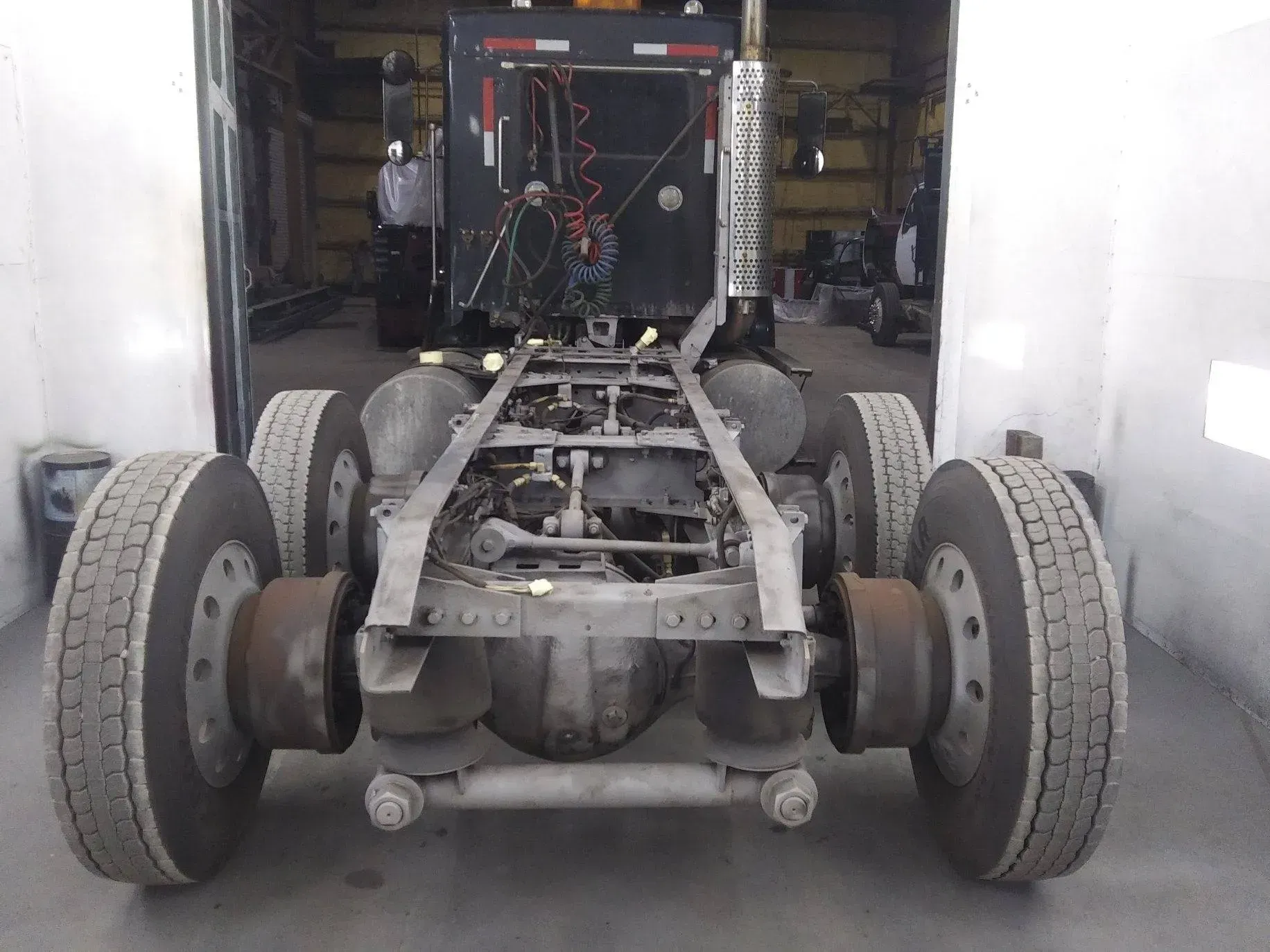 Undercarriage of a semi-truck inside a garage; visible wheels, frame, and suspension.