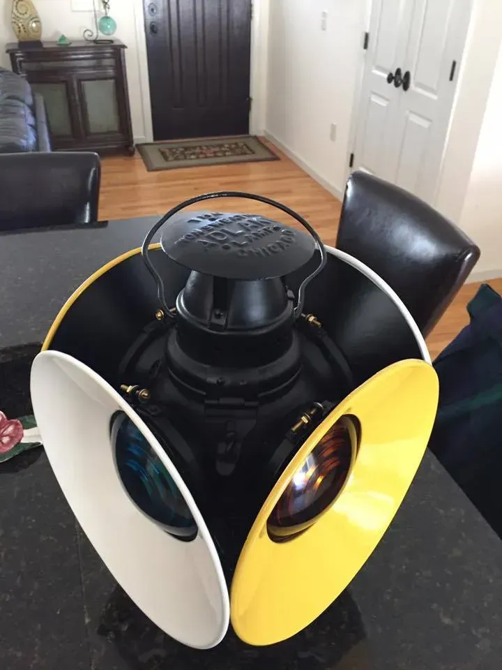 Black, antique train lantern with white and yellow signals on a table.