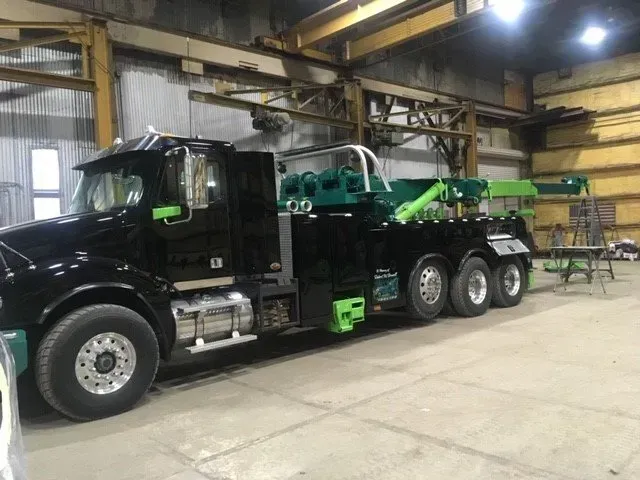 Black tow truck with green accents parked inside a warehouse.