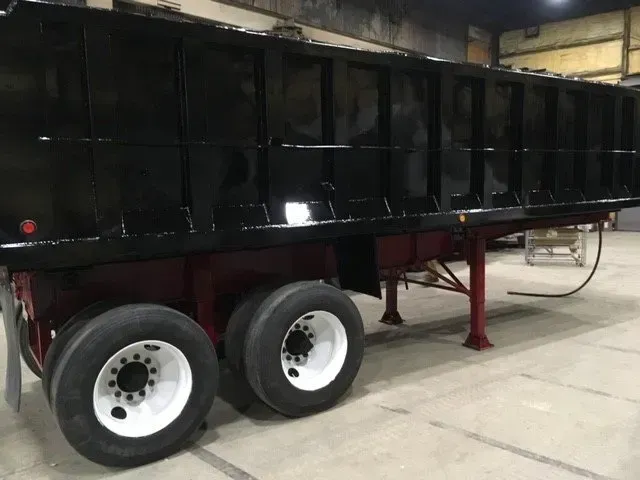 Black dump trailer with white-rimmed tires, red frame, and gray surroundings.