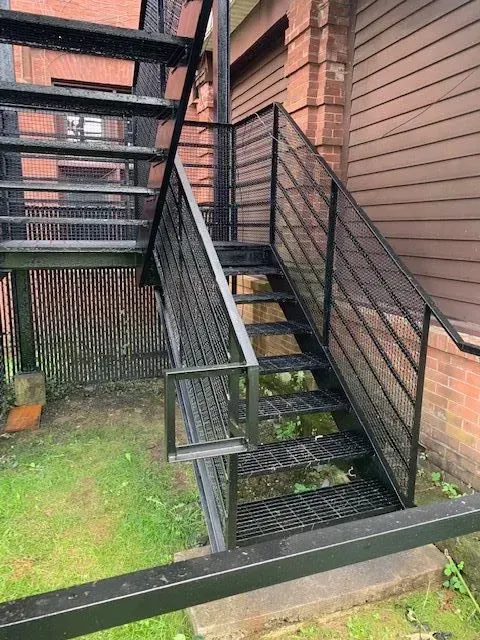 Black metal outdoor staircase against a brick and wood building.