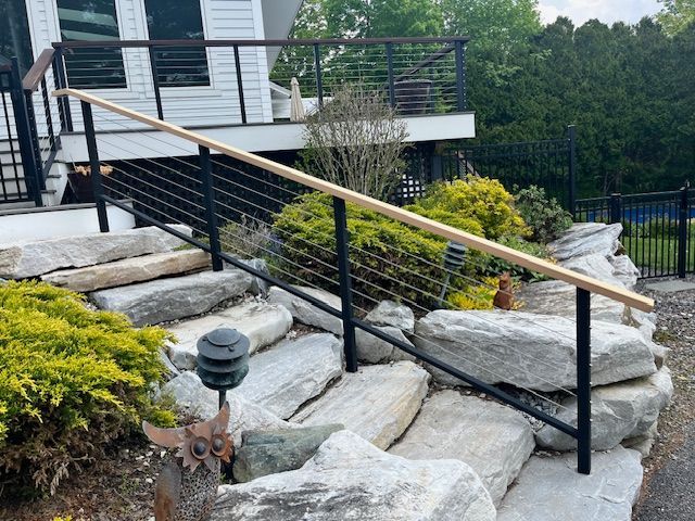 Black metal railing with cable infill and wooden handrail on stone steps.