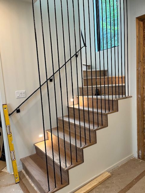 Staircase with wooden steps and black vertical railings. Handrail on the left. Cream walls and light colored floors.
