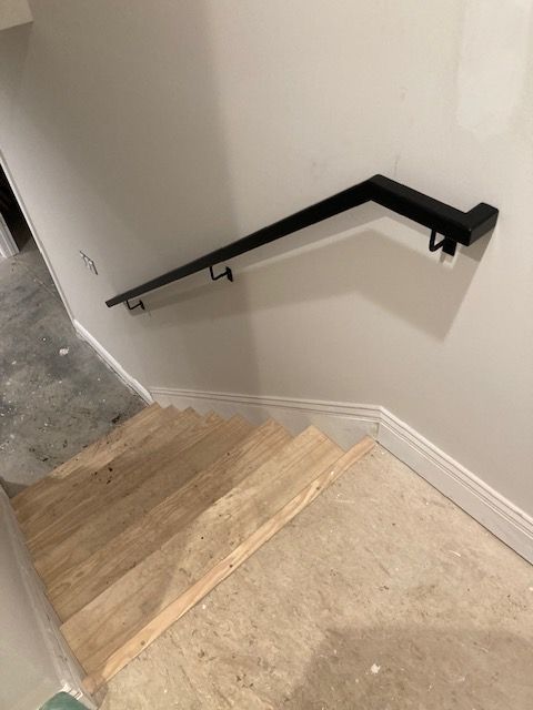 Black metal handrail on a white wall above wooden stairs in a construction setting.