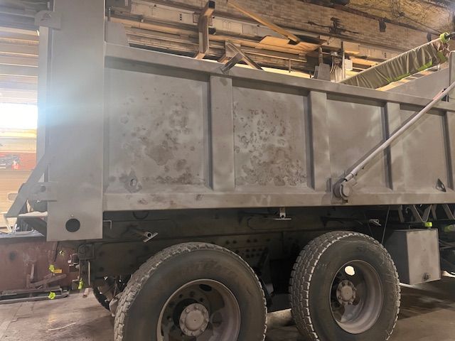 Person in protective suit using a tool, likely for industrial cleaning or painting, in a metallic setting.