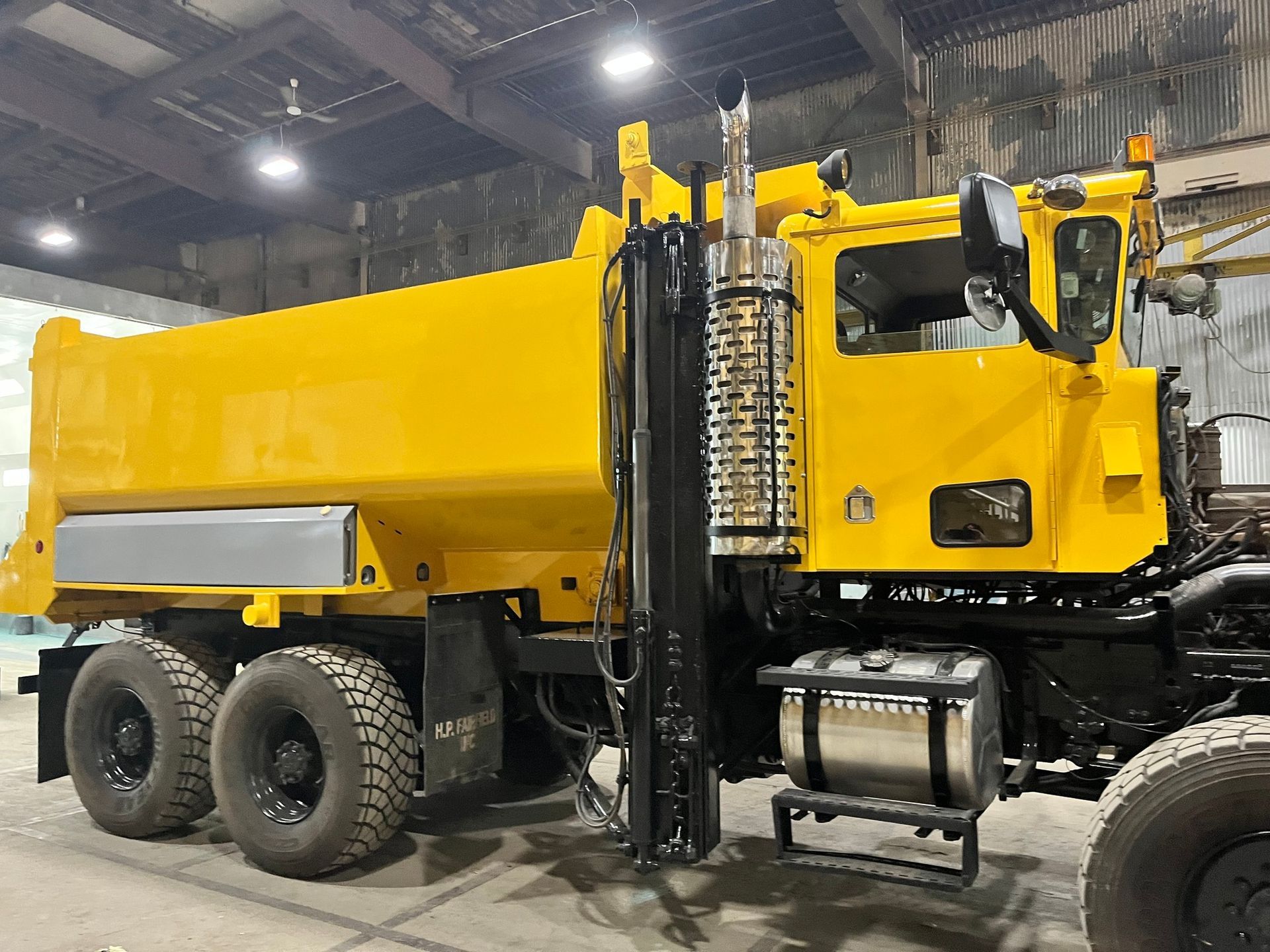 Yellow dump truck with black frame and wheels, in a warehouse.