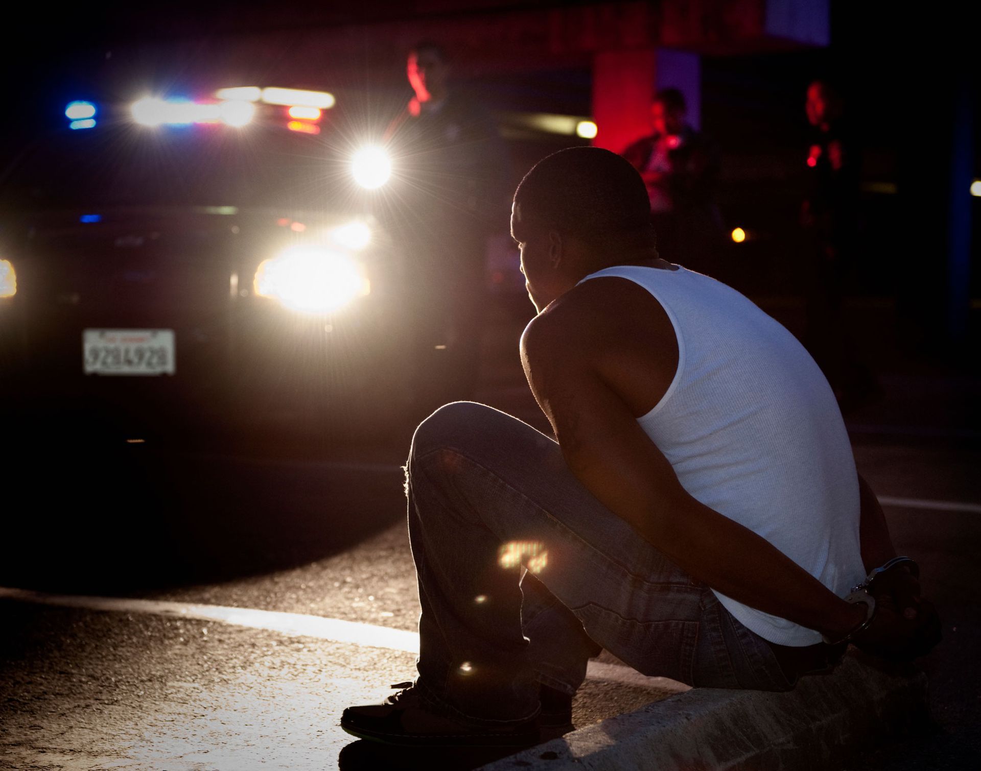 A man sits on the side of the road in front of a police car