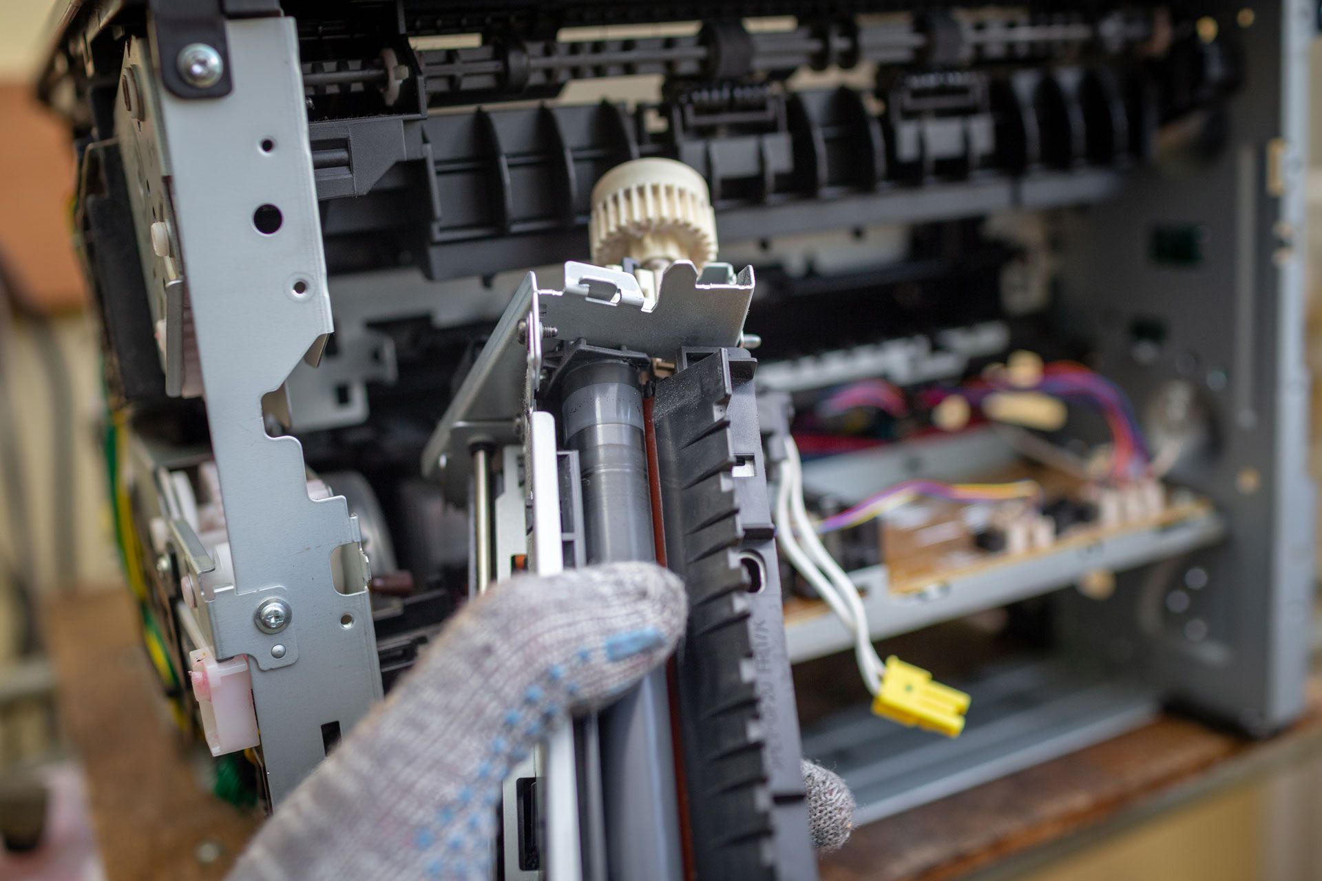 Person wearing a glove holding a printer component from an open printer with exposed internal components.