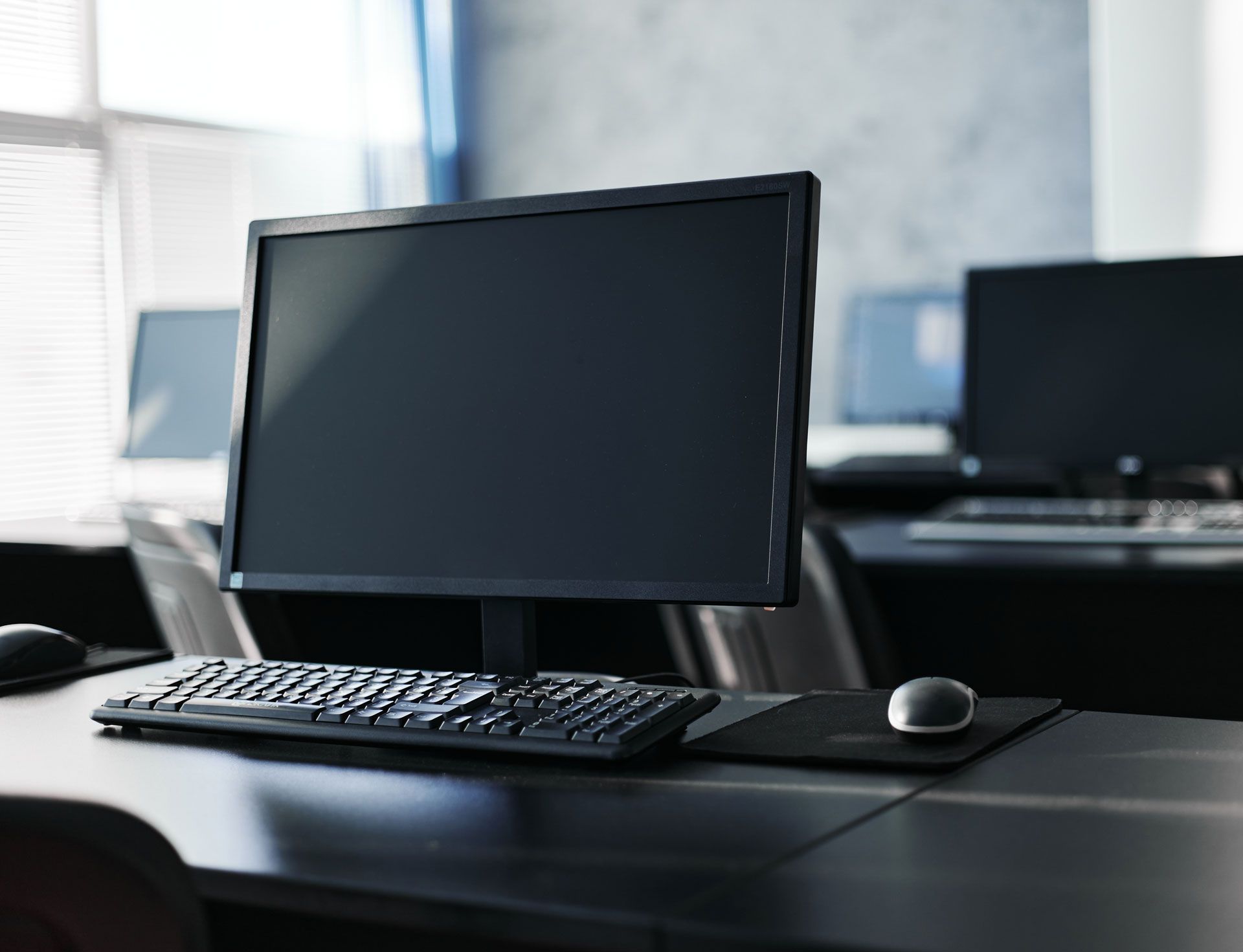 Computer workstation in a classroom setting with a monitor, keyboard, and mouse on a desk.