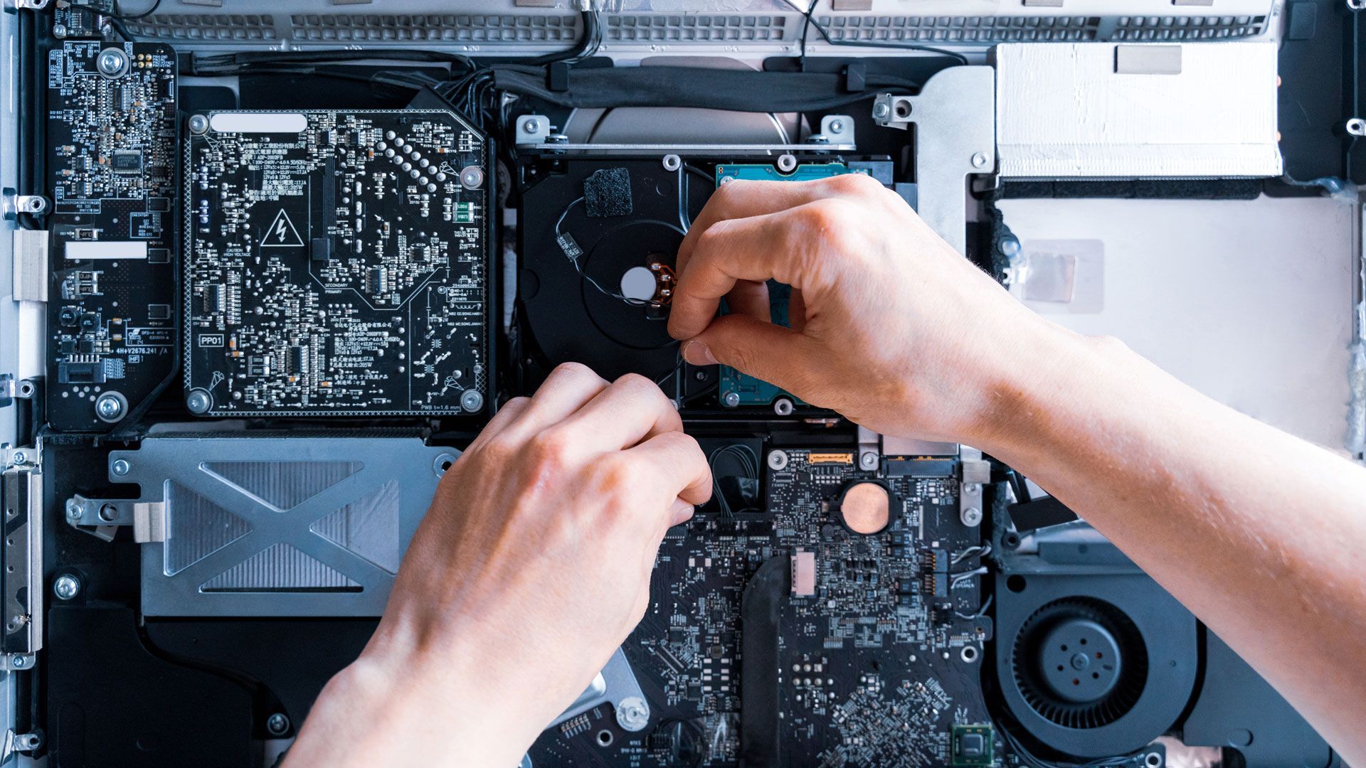 Hands installing a component inside a computer, showing internal circuit boards and hard drive.