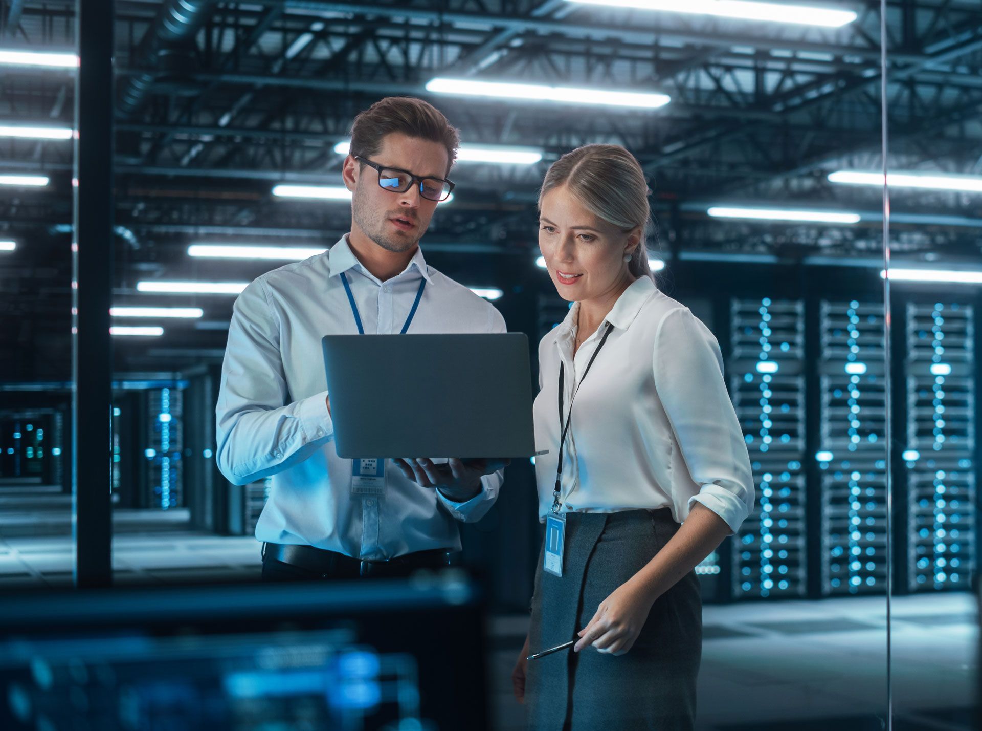 Two IT professionals looking at a laptop in a data center.