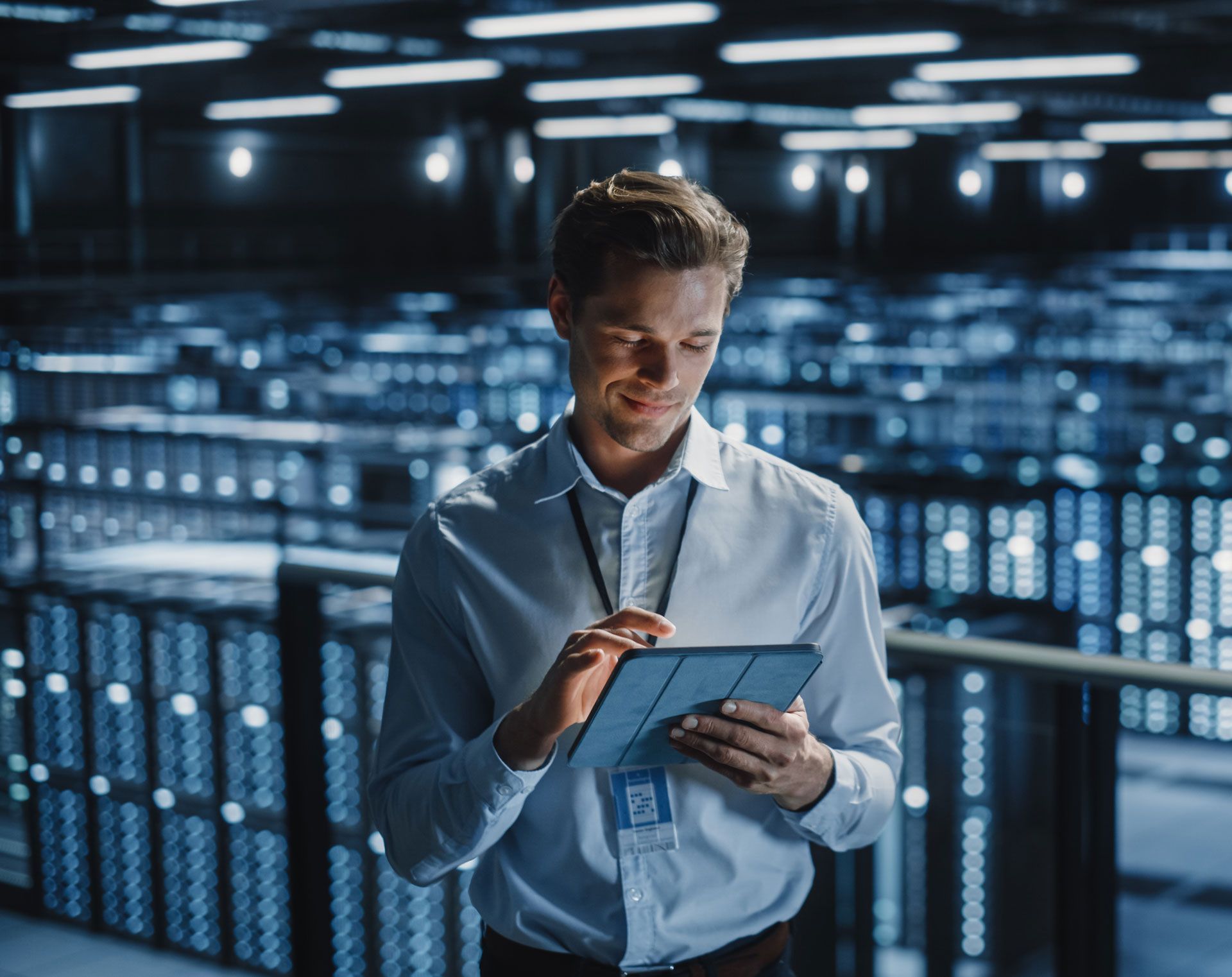 Man in a data center, using a tablet, smiling. Racks of servers in the background.