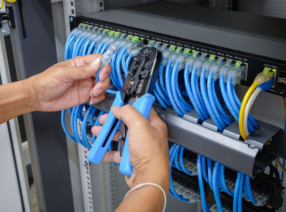 Person connecting blue network cables to a rack-mounted server with crimping tool.