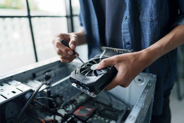 Person installing a computer graphics card with a screwdriver in an open desktop case.