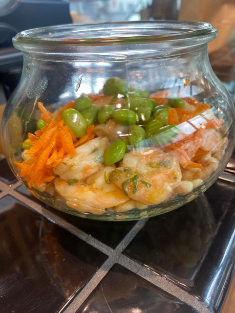 Piatto di cibo con pomodori e formaggio su un tavolo, accanto a un bicchiere, una bottiglia e una pianta.