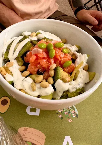 Ciotola con salmone, avocado, edamame e condimento su una tovaglietta verde.