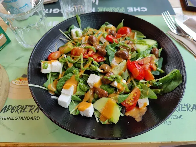 Insalata in una ciotola nera: verdure, pomodori, formaggio, olive e condimento, sul tavolo di un ristorante.