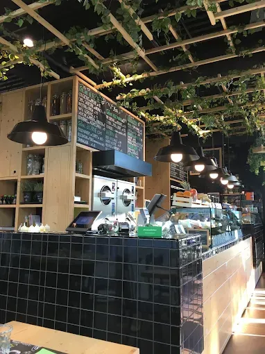 Interno di un bar con bancone in piastrelle nere, menù, luci sospese e decorazioni con piante.