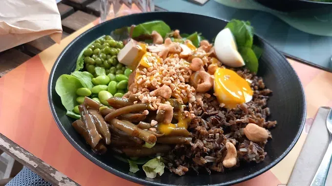 Insalatiera con vari ingredienti colorati, tra cui verdure, uova e noci, in una ciotola scura su un tavolo.