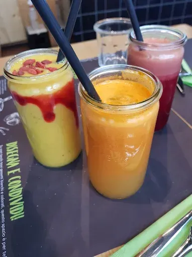 Tre succhi colorati in barattoli di vetro con cannucce su un tavolo.