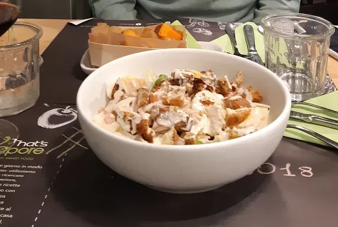 Ciotola di insalata condita, in un ambiente da ristorante, con patatine fritte sullo sfondo.