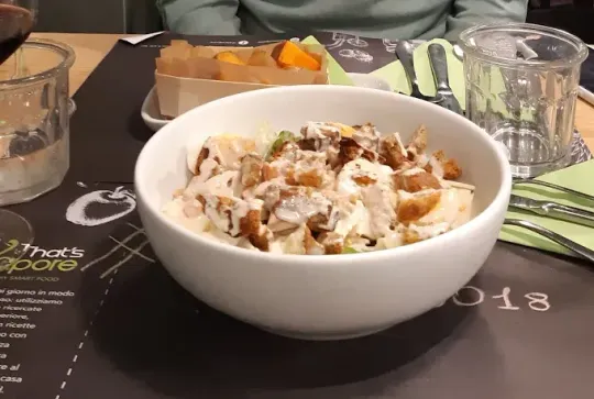 Ciotola di insalata condita, in un ambiente da ristorante, con patatine fritte sullo sfondo.