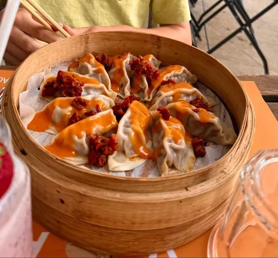 Ravioli in una vaporiera di bambù, conditi con salsa, su un tavolo all'aperto.