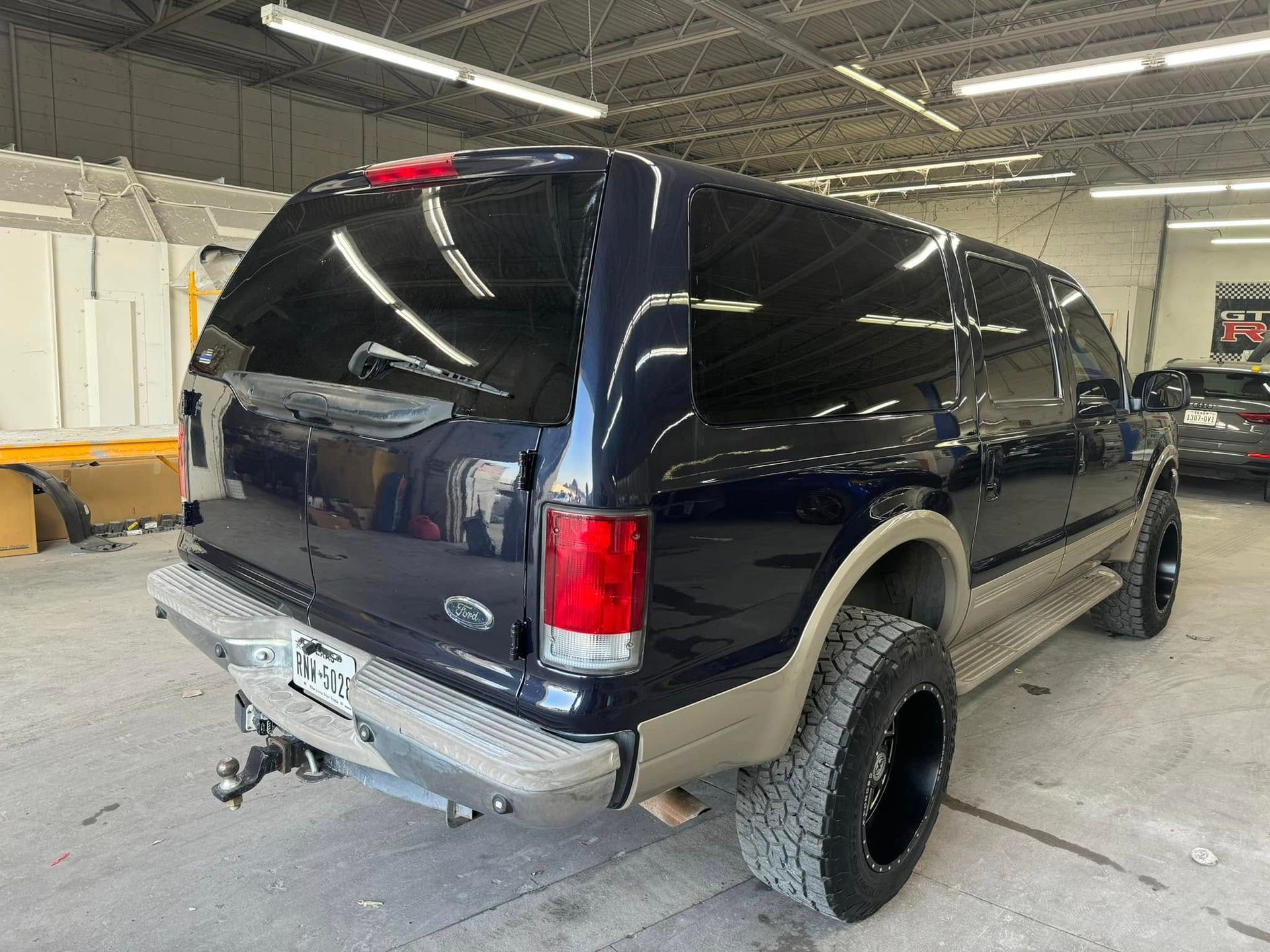 Dark blue Ford Excursion SUV, rear view, in a garage. Tan lower body panels, black wheels.