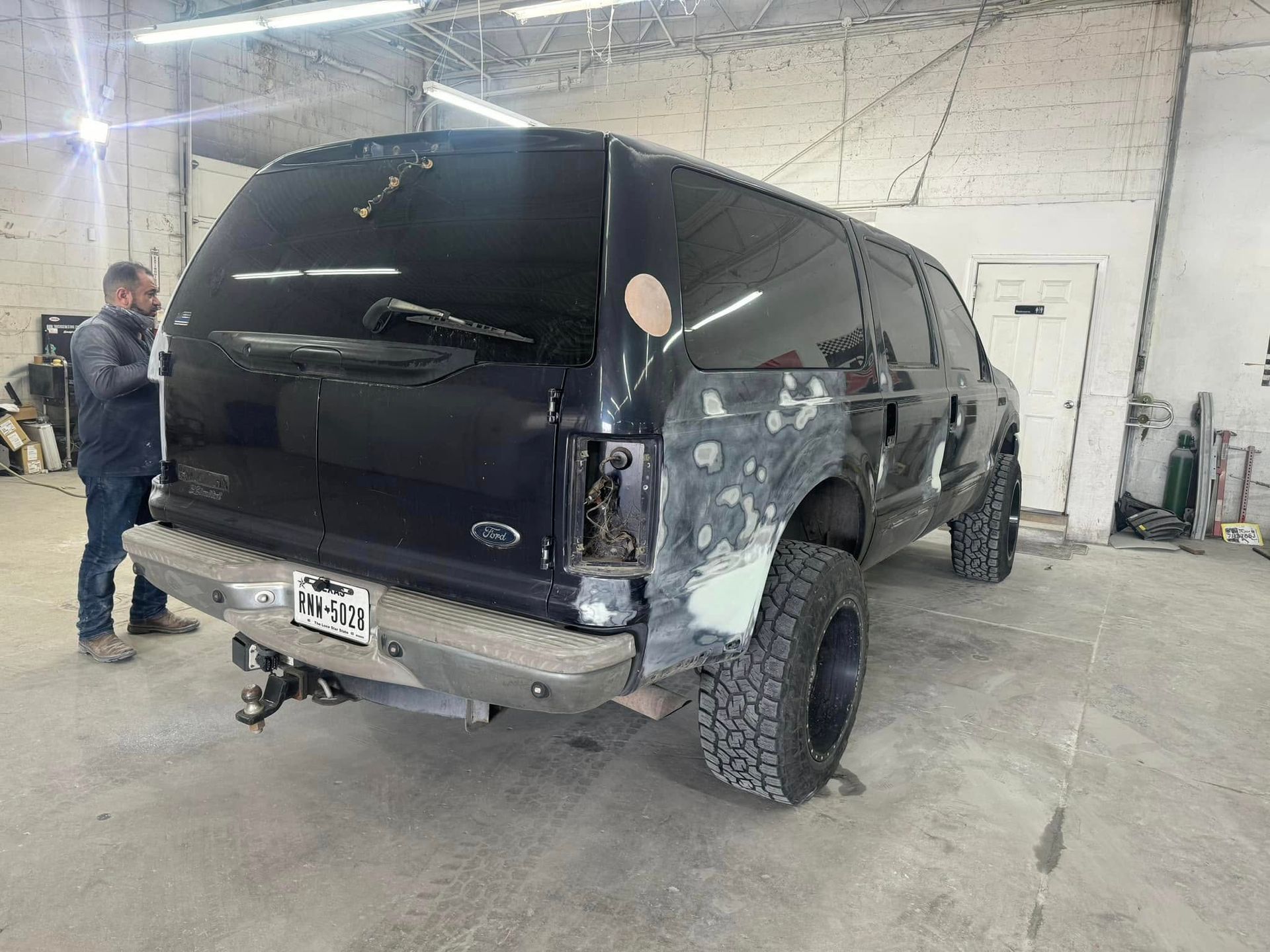 A man working on a black SUV in a workshop. The vehicle has damage and repairs in progress.