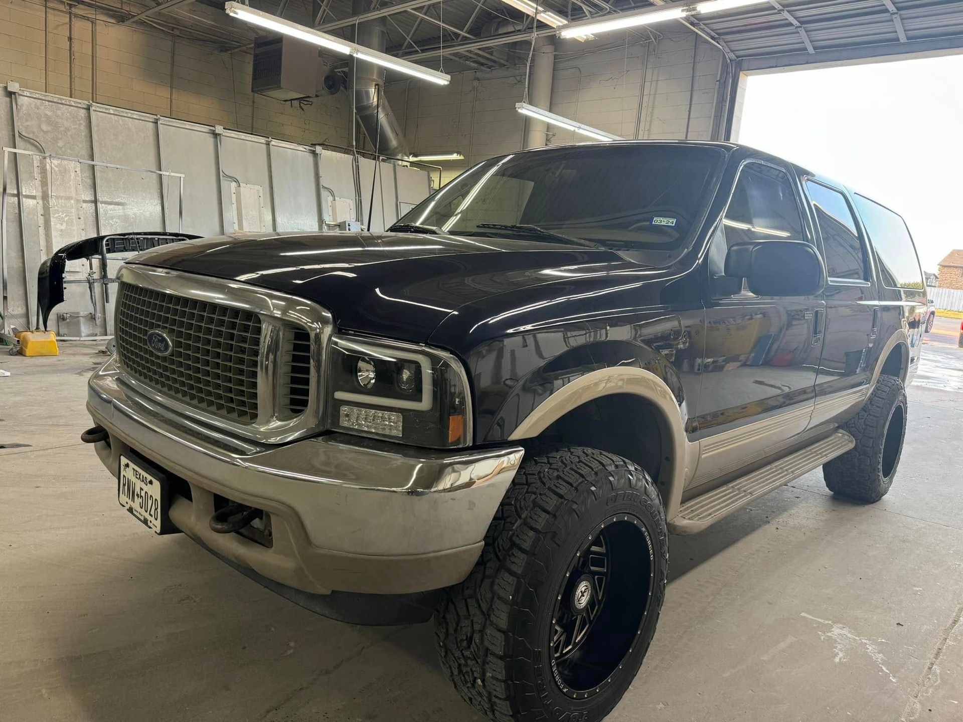 Black Ford Excursion SUV with chrome trim and black wheels parked inside a shop.