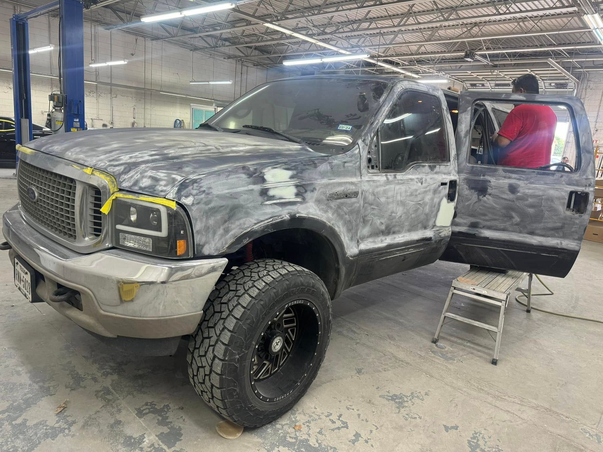 A gray pickup truck in a garage, being worked on. A person is in the open driver's side door.