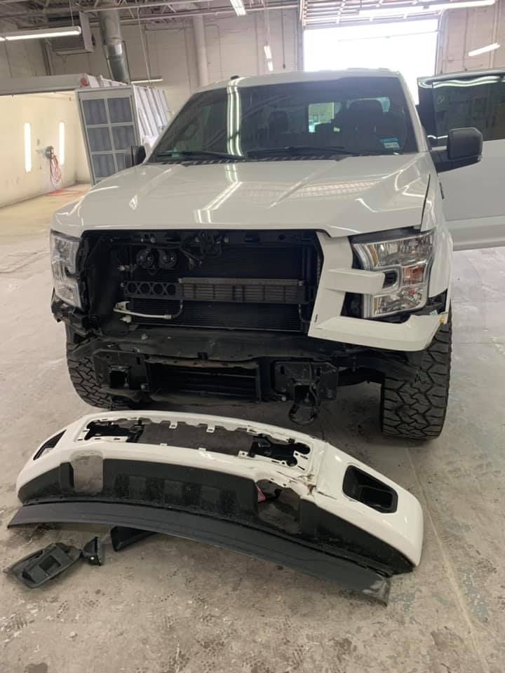 White Ford pickup truck with front bumper removed in a repair shop.