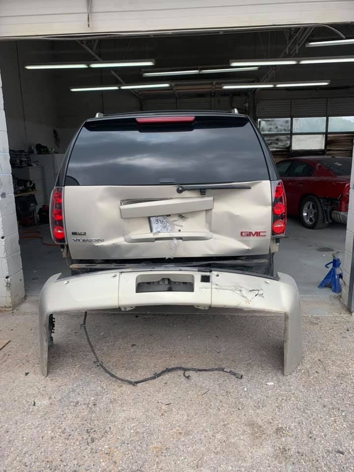 Damaged gold GMC Yukon SUV with detached bumper in a garage.
