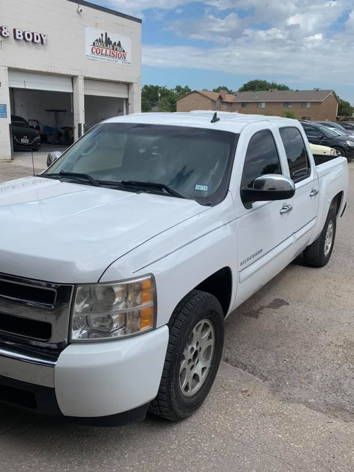 White Chevrolet pickup truck parked outside a body shop on a sunny day.