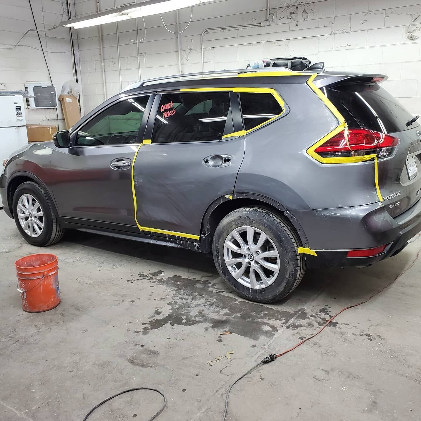 Gray SUV, bodywork in progress, masked with yellow tape in a garage setting.