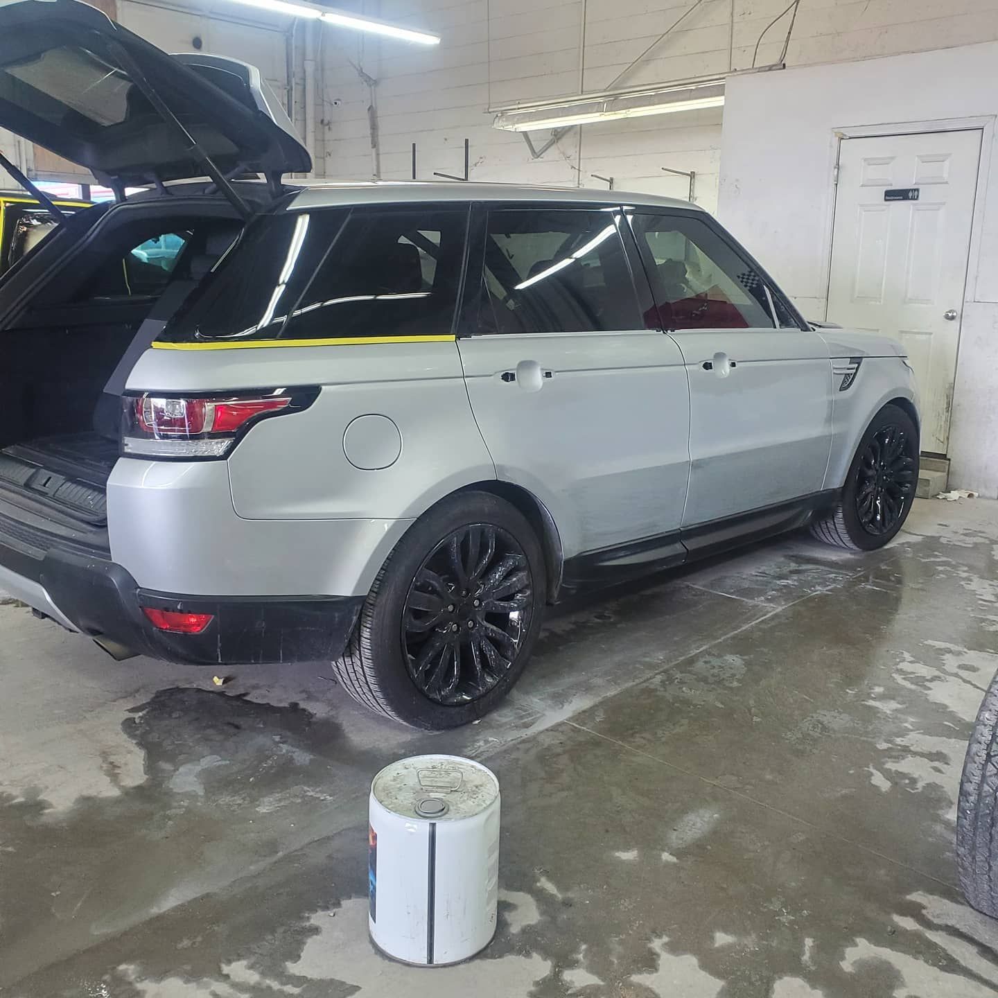 Silver Range Rover Sport with black wheels and open trunk in a garage.
